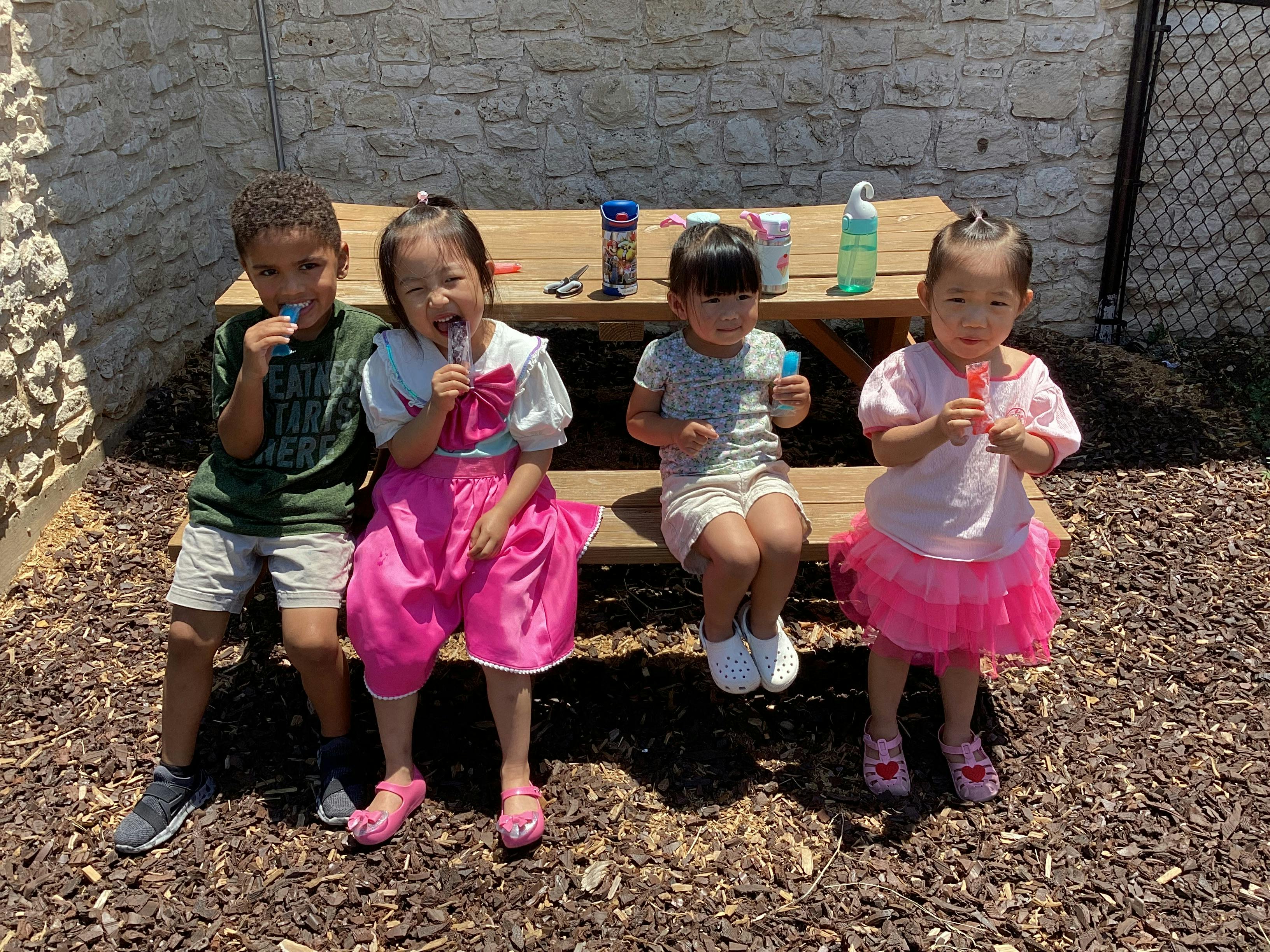 Four children eating popsicles on a picnic bench