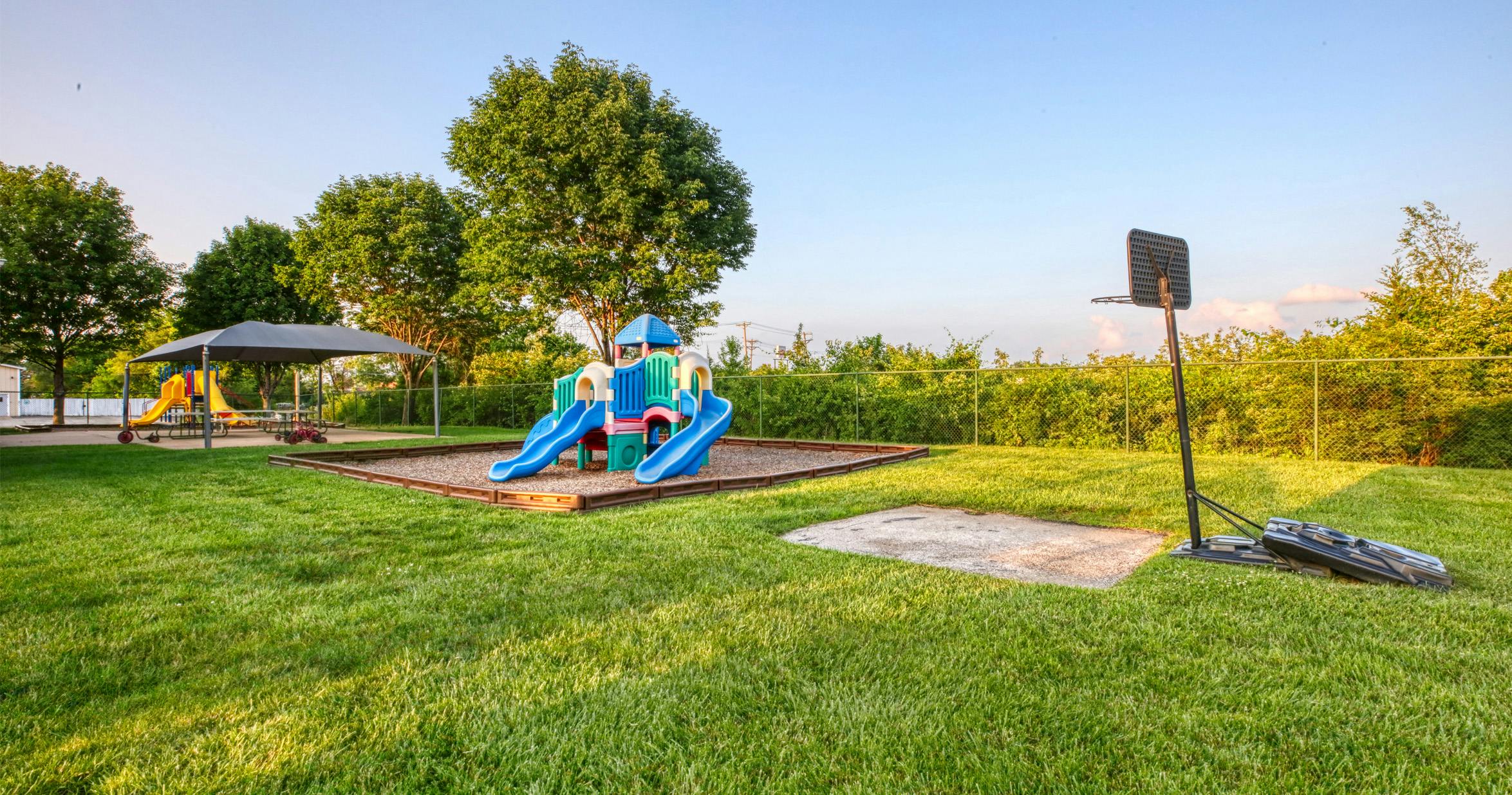 Playground area with slides, a covered picnic table, and a basketball hoop