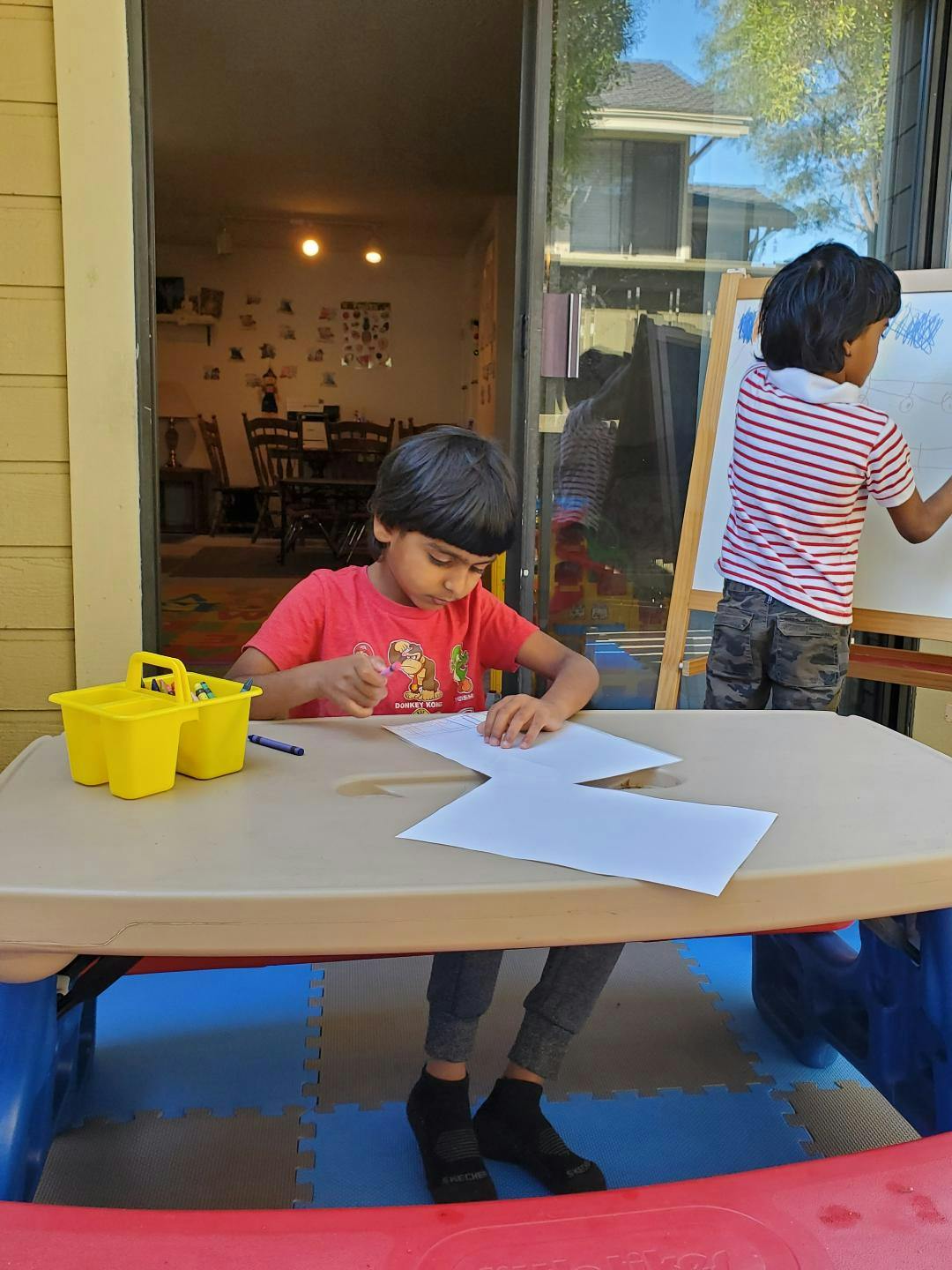 Two children drawing, one at a table and one at an easel