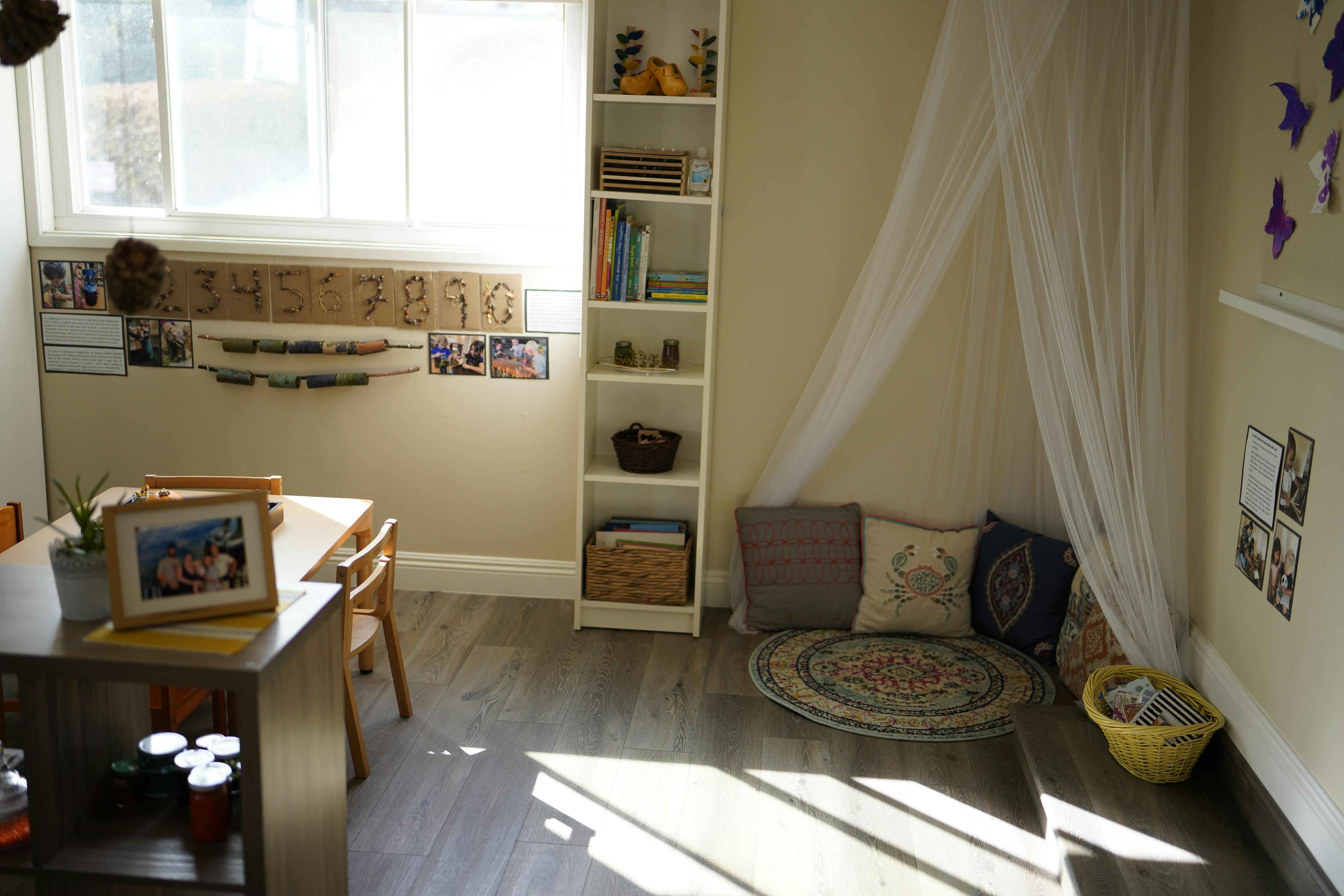 Room with a table and chairs, a bookshelf, and a floor cushion with pillows
