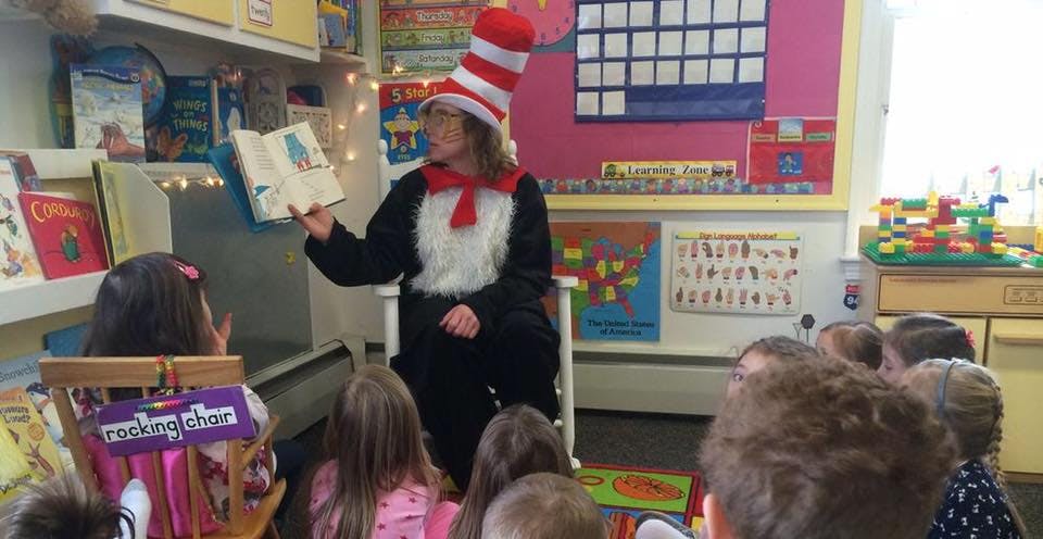 Person in striped hat reading a book to children in a classroom