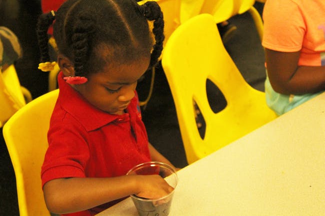 Child in red shirt sitting at a table with a cup