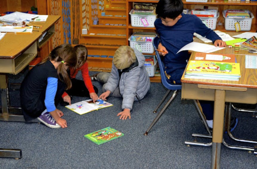 Children looking at books on the floor and at a desk in a classroom