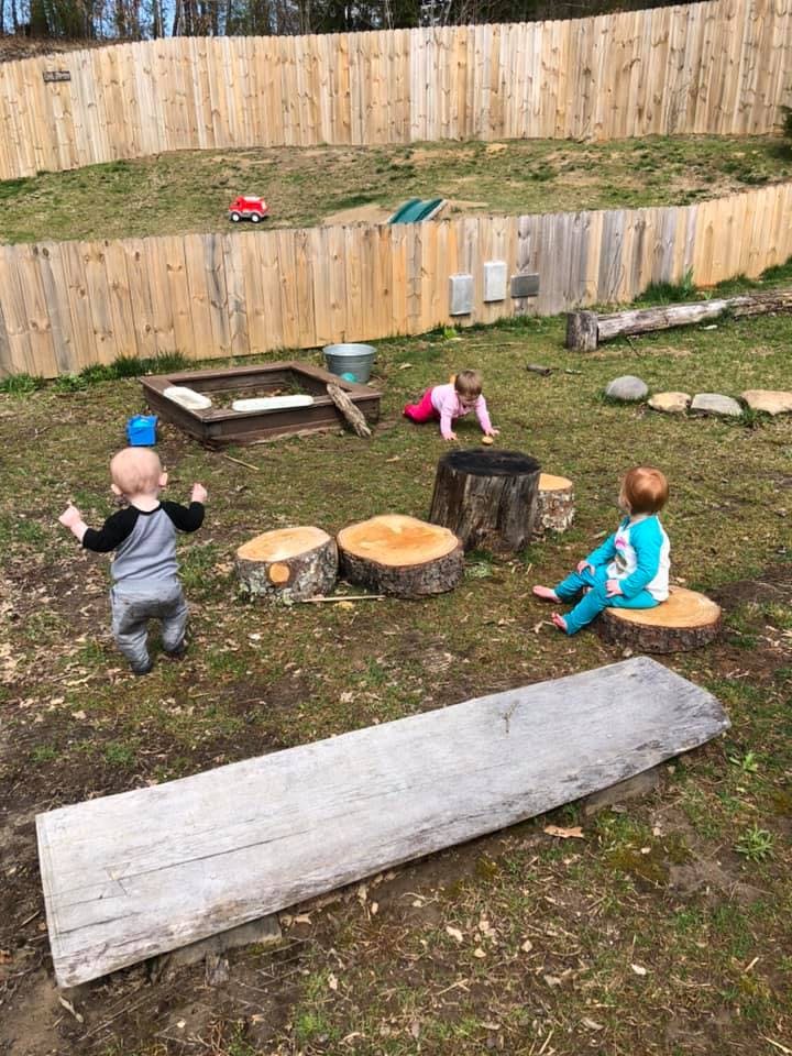 Three children playing outdoors with tree stumps and a wooden fence