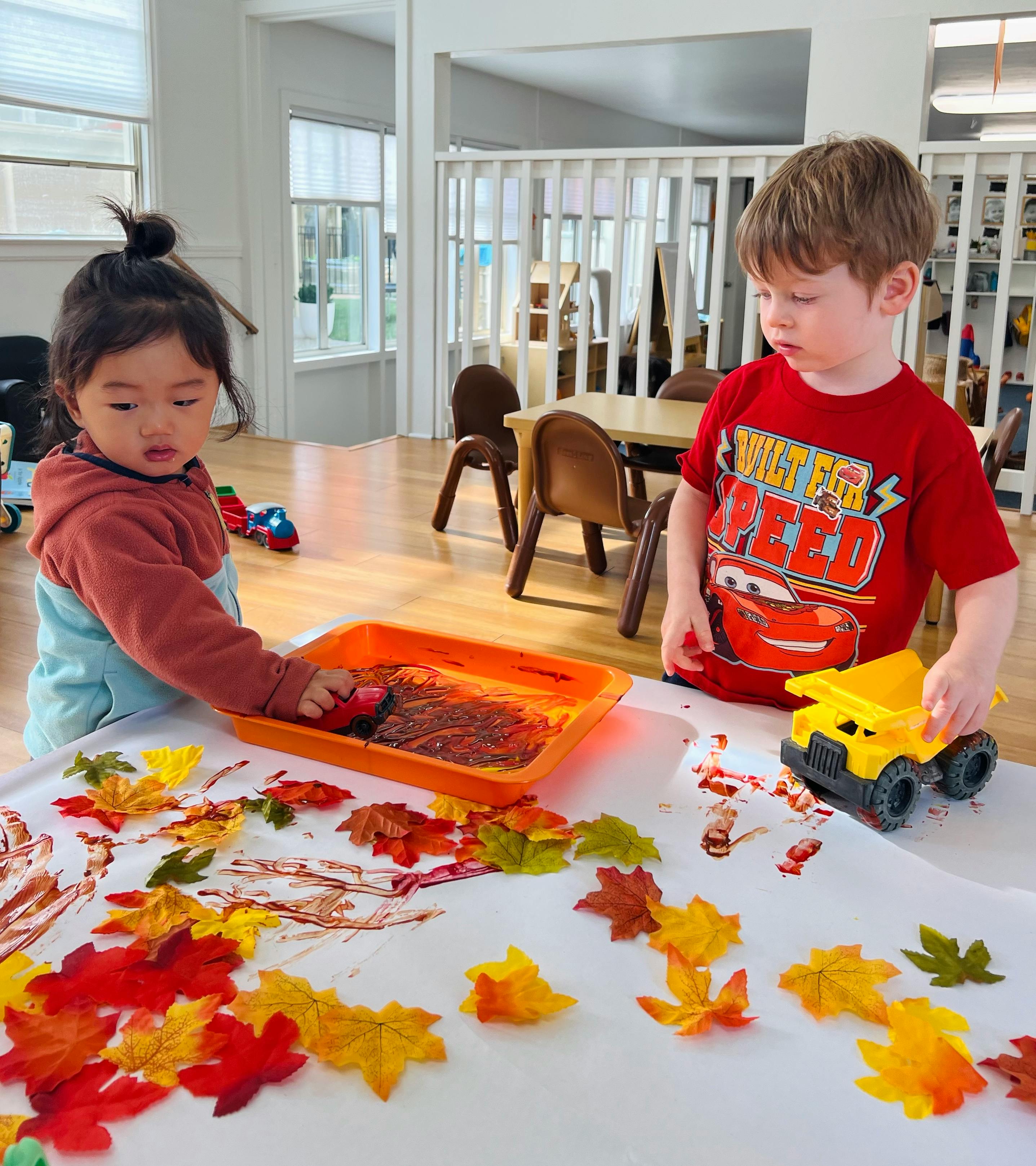 Two children playing with paint and autumn leaves on a table