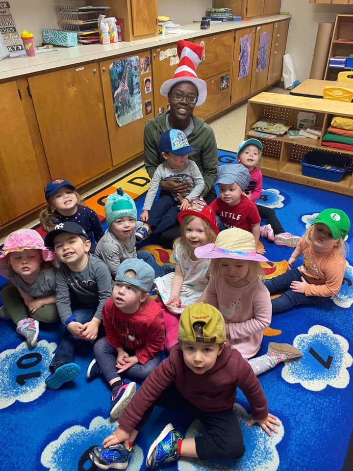 Person in a striped hat with multiple children in a classroom