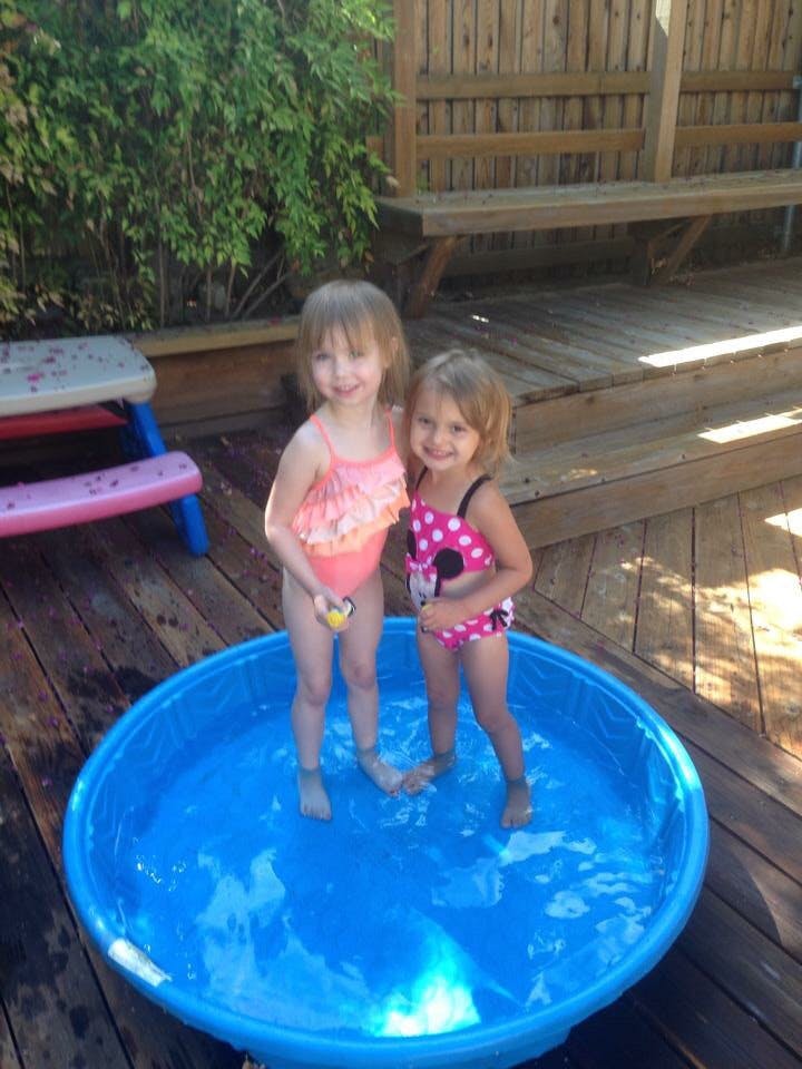 Two children in swimsuits standing in a blue wading pool