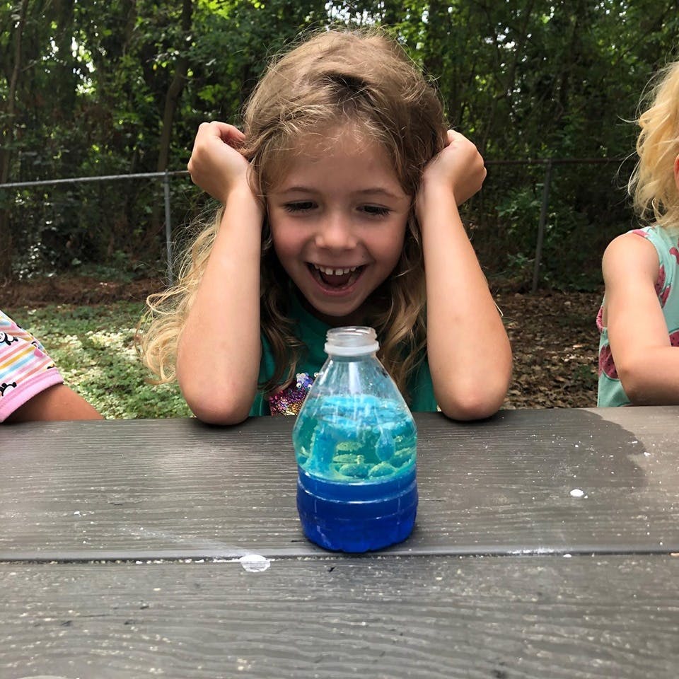 Child looking at a bottle with blue liquid and objects inside a clear top on a table