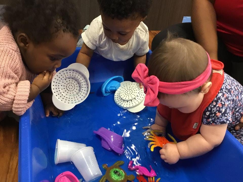 Three children playing with toys in a blue water table