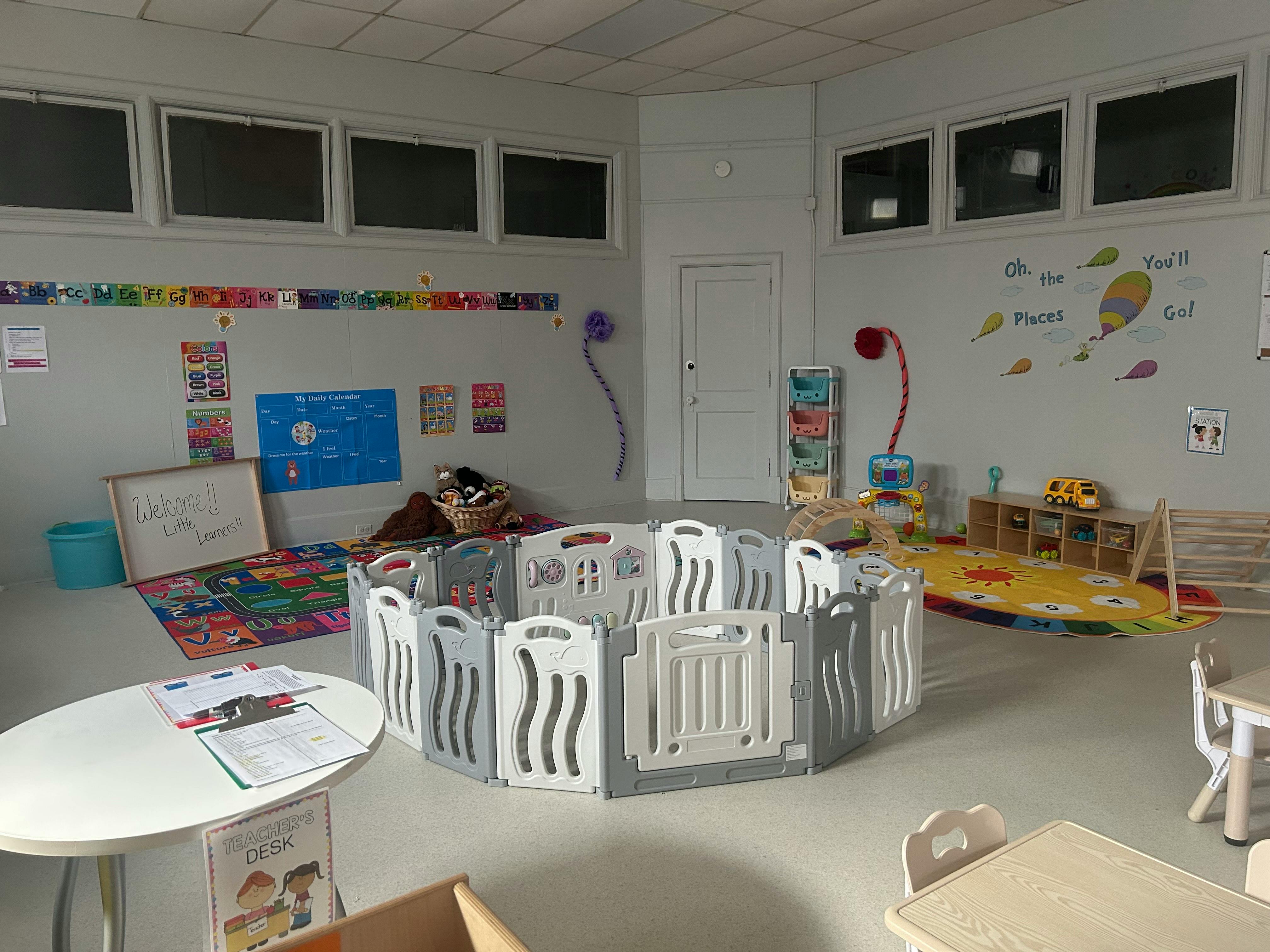 An empty early childhood classroom with a playpen, colorful rugs, and learning charts