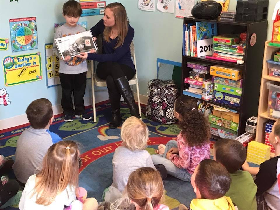 Adult showing a book to a child while other children sit on the floor