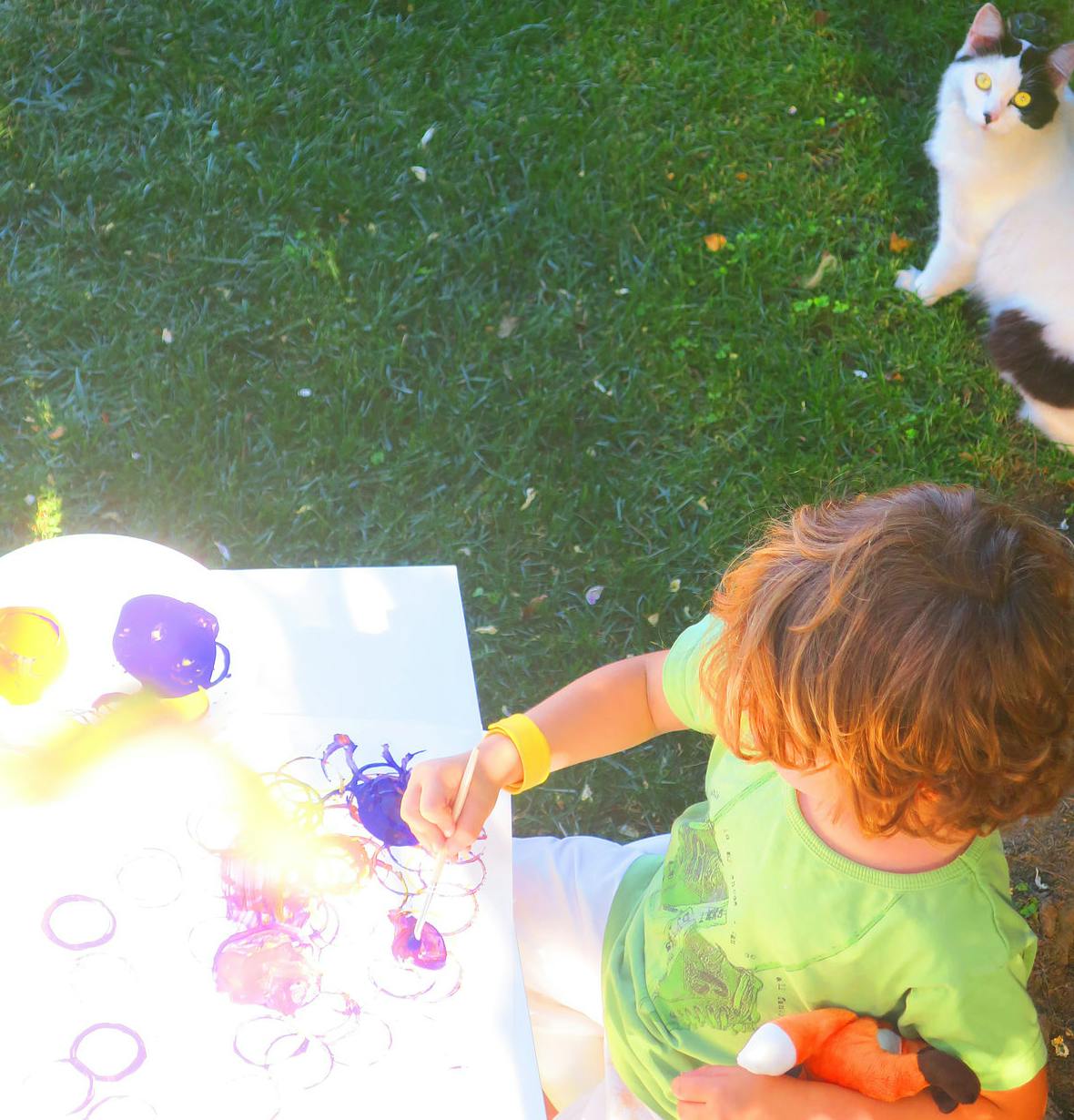 Child painting at a table outdoors with a cat nearby