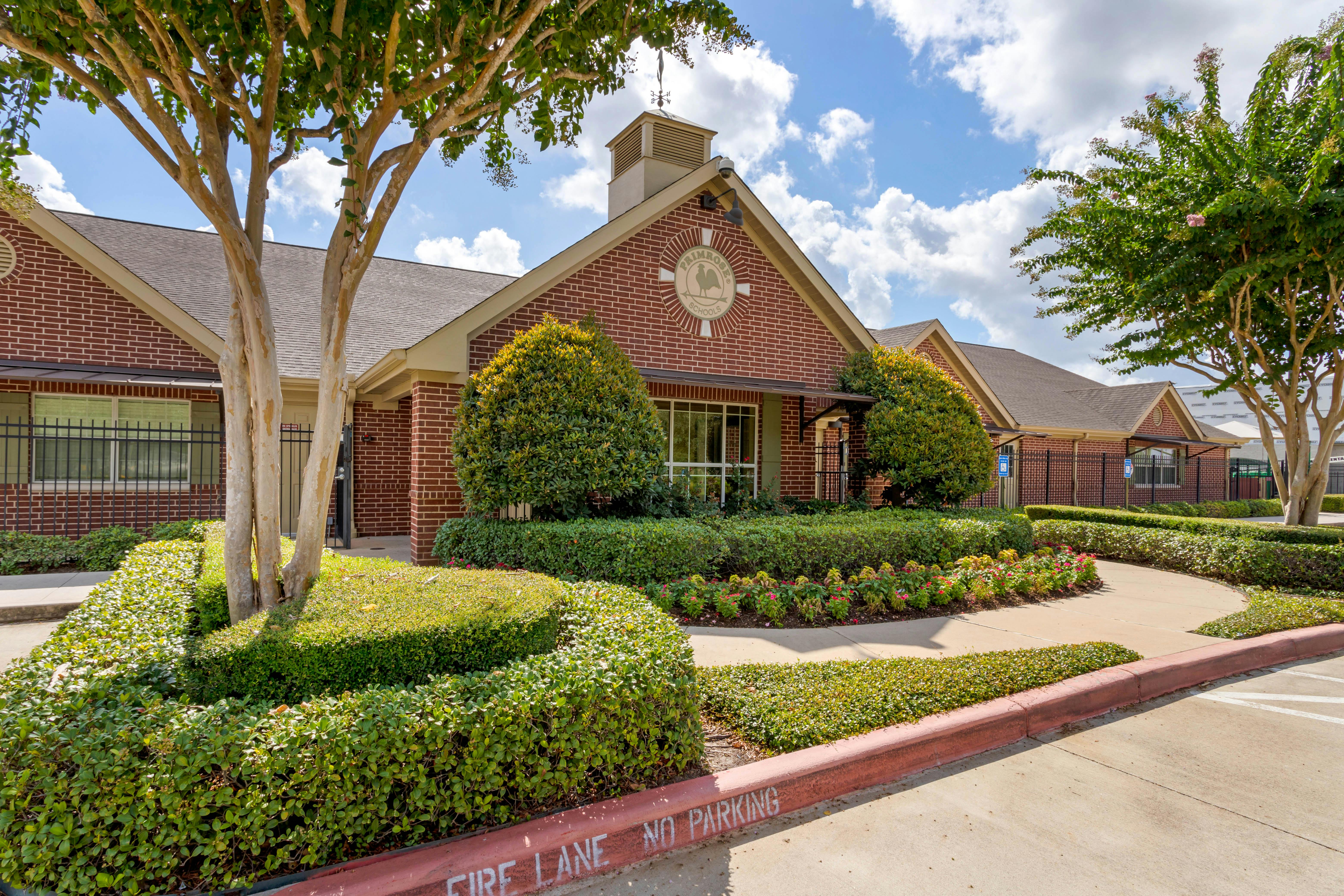 Brick building with a logo that says Primrose Schools and manicured hedges