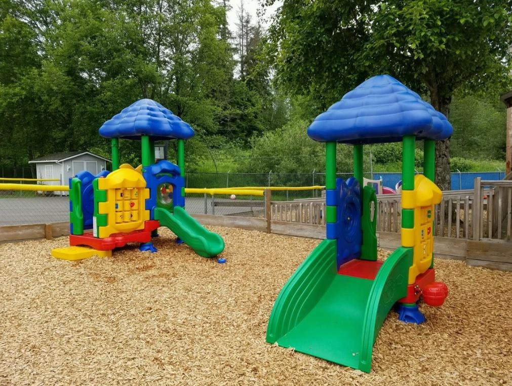 Two colorful playground structures with slides on wood chips