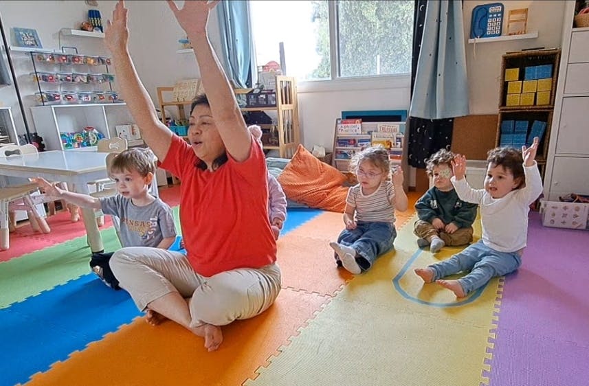 Person and children sitting on floor with arms raised