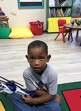 Child sitting on floor with toy helicopter in a classroom