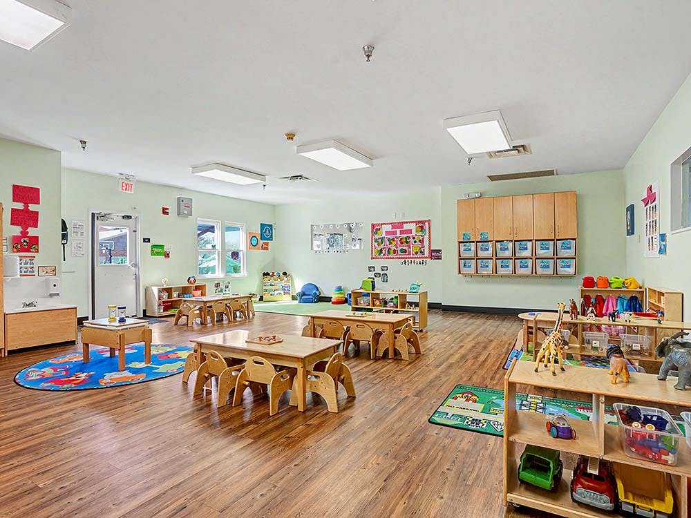 Empty preschool classroom with small tables and chairs, play mats, and toys