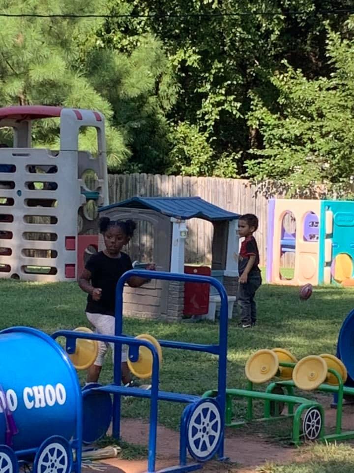 Two children playing on a playground with playhouses and ride-on toys
