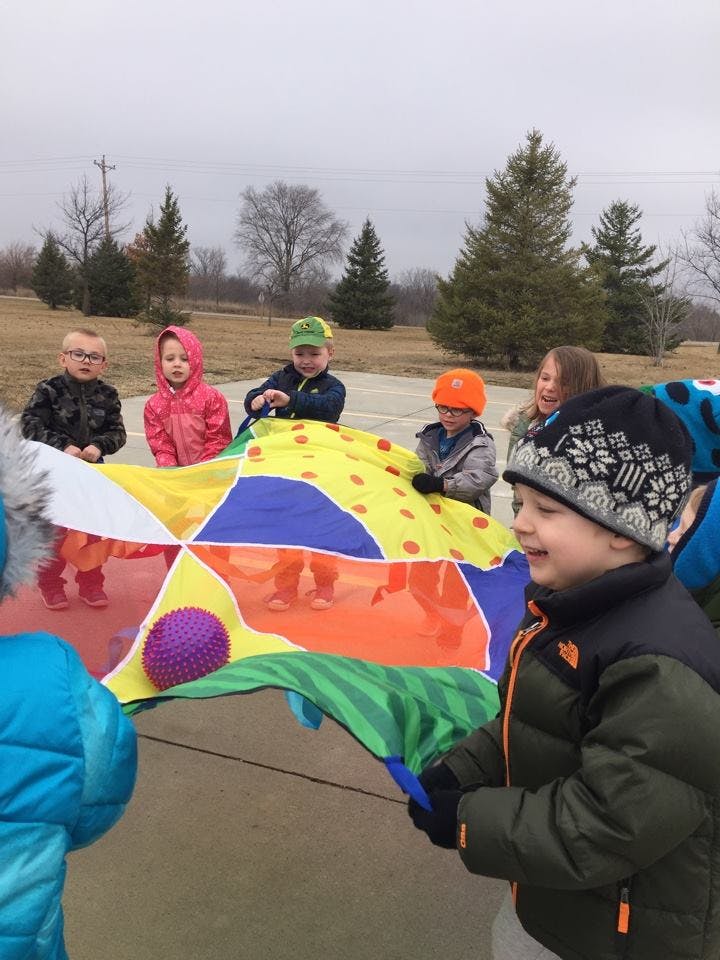Children playing with a colorful parachute and a purple ball outdoors