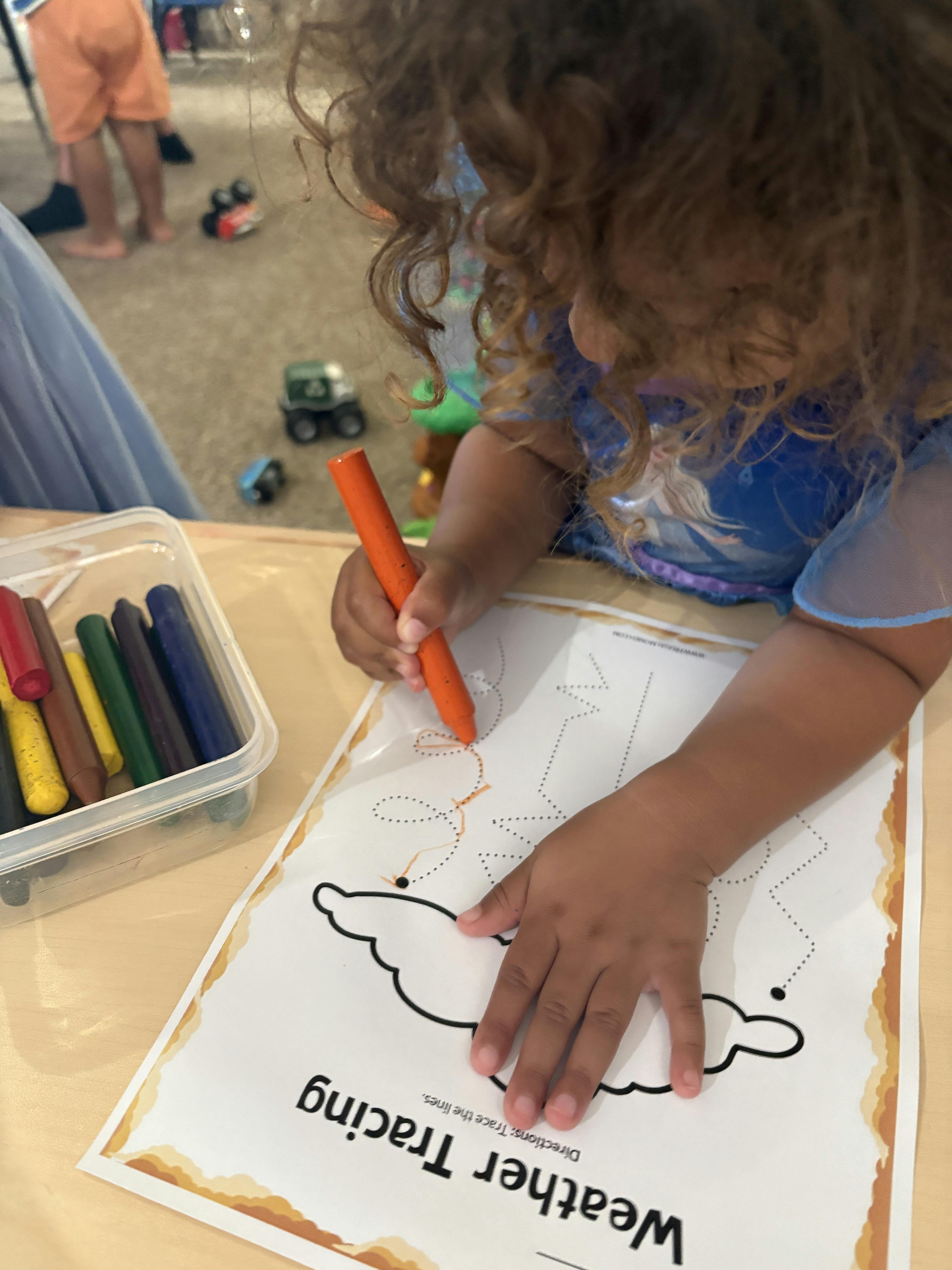 Child tracing lines on a weather worksheet with an orange crayon