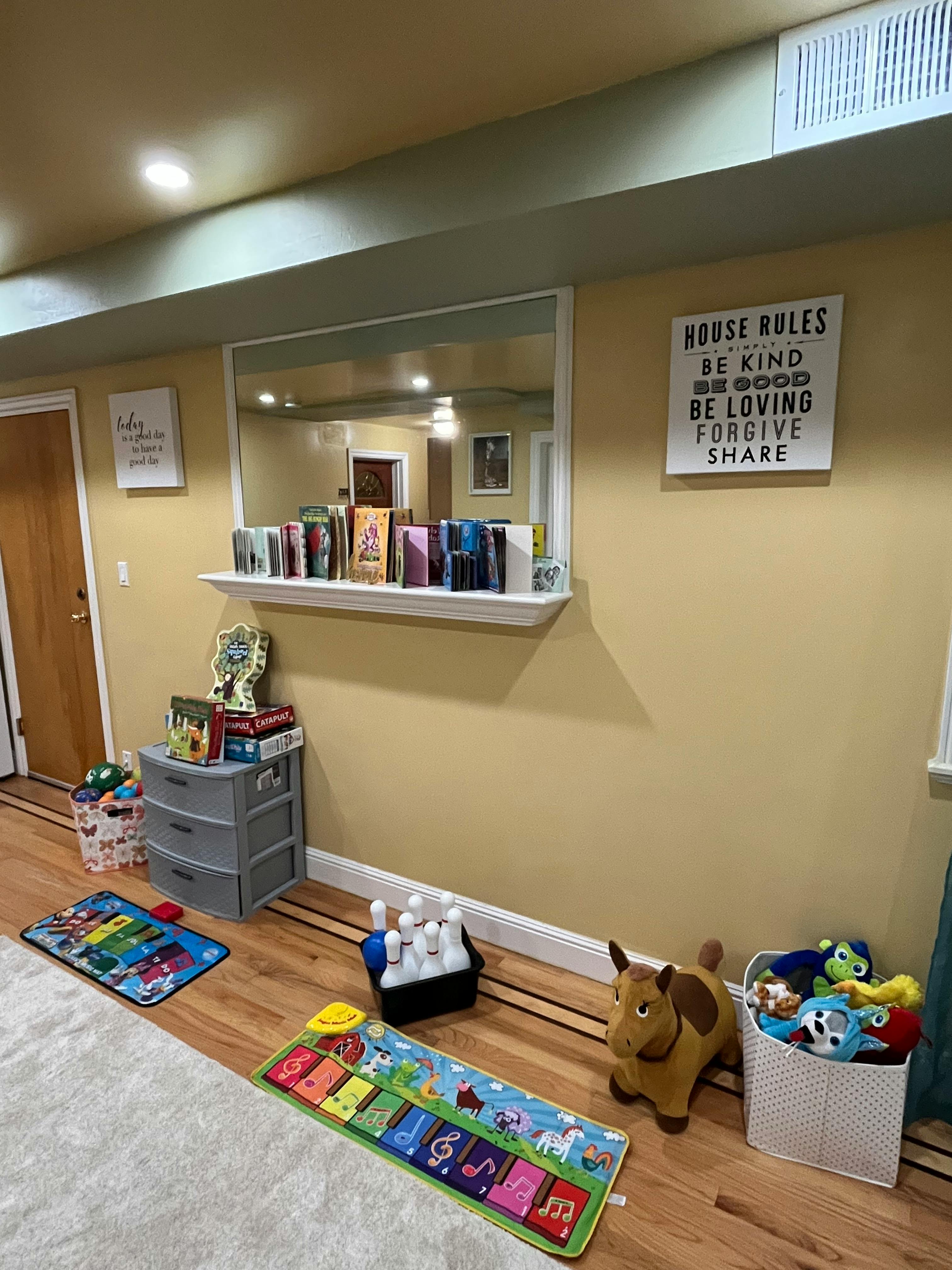 Playroom with toys on the floor and a shelf of books above a dresser