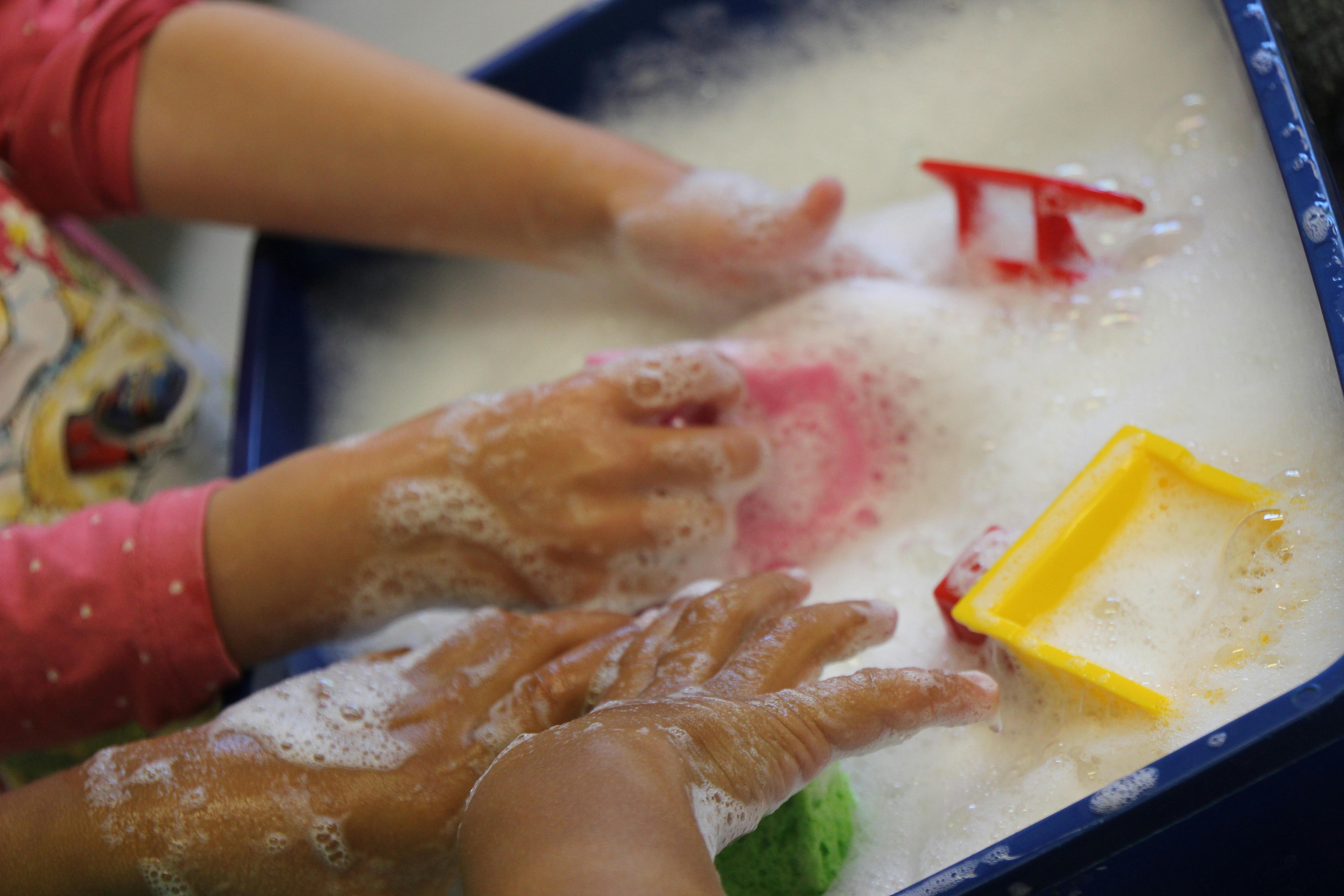 Children's hands playing in soapy water with toys