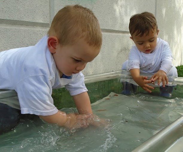 Two children playing with water in a container