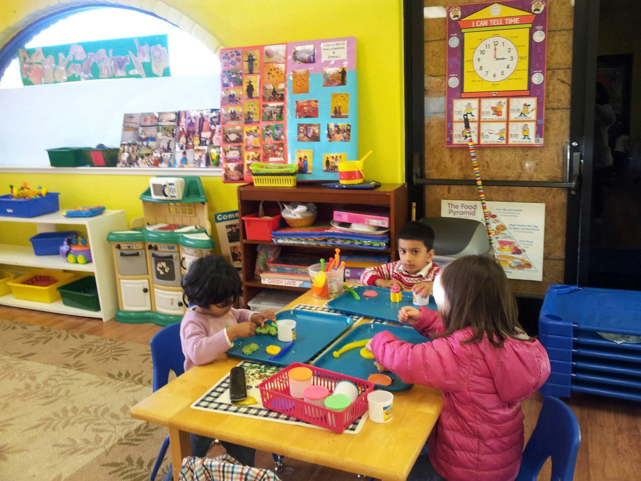 Three children playing with toys at a table in a classroom