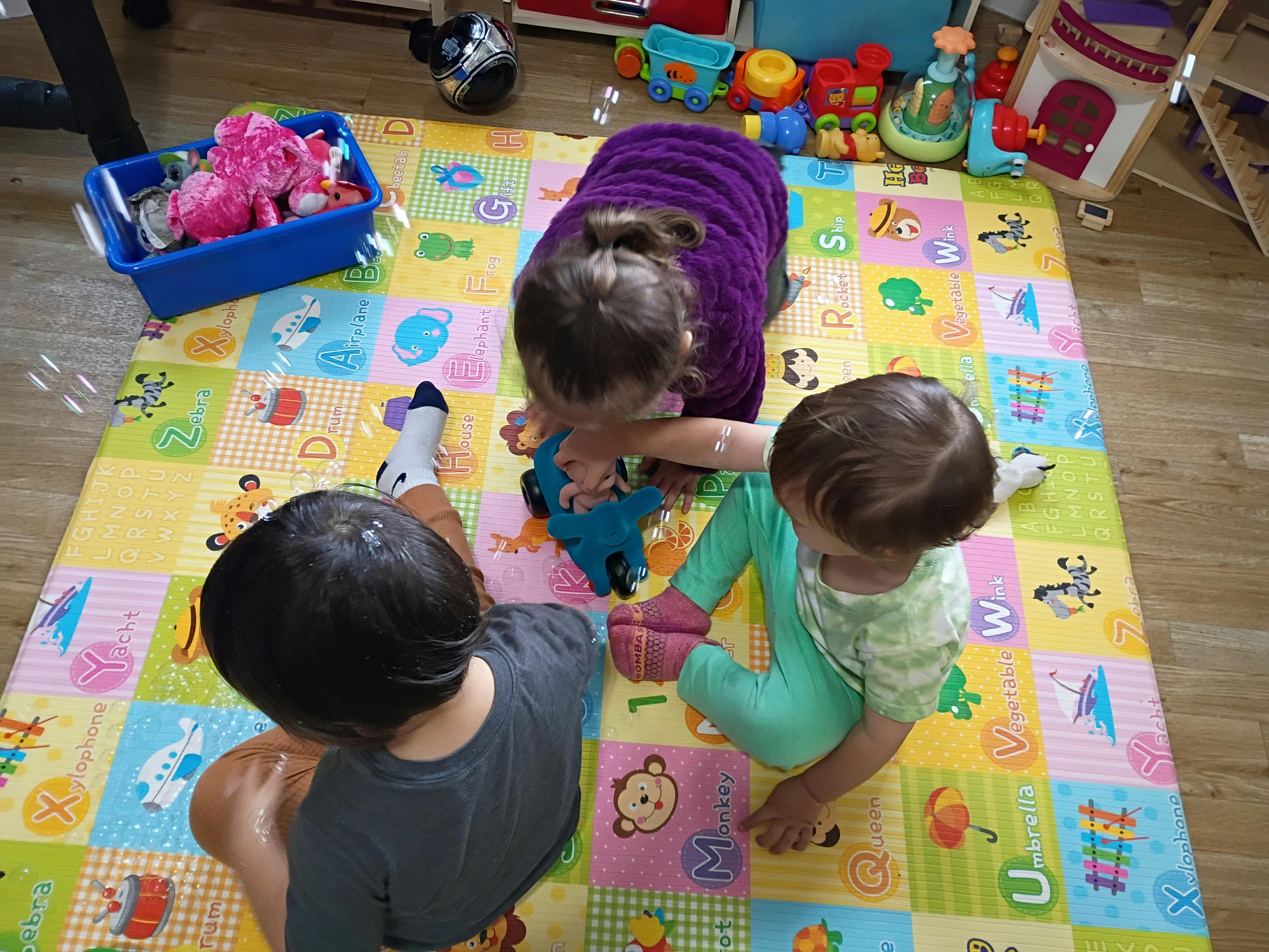 Three children playing with toys on an alphabet play mat