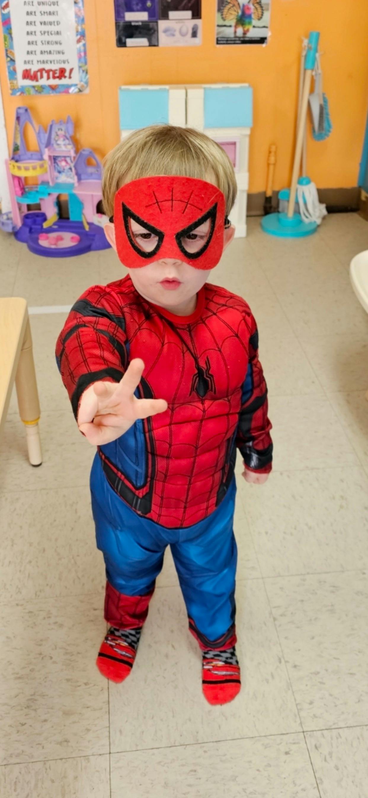 Child in a Spider-Man costume with a mask, holding up two fingers