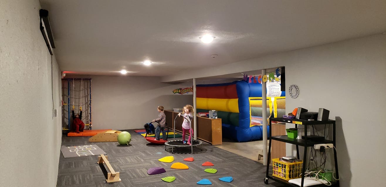 Two children playing on a trampoline and balance board in a room with an inflatable