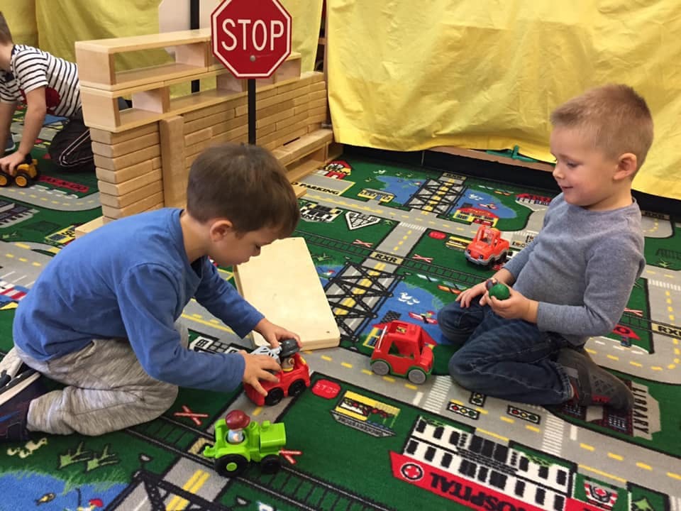 Two children playing with toy trucks on a road map rug