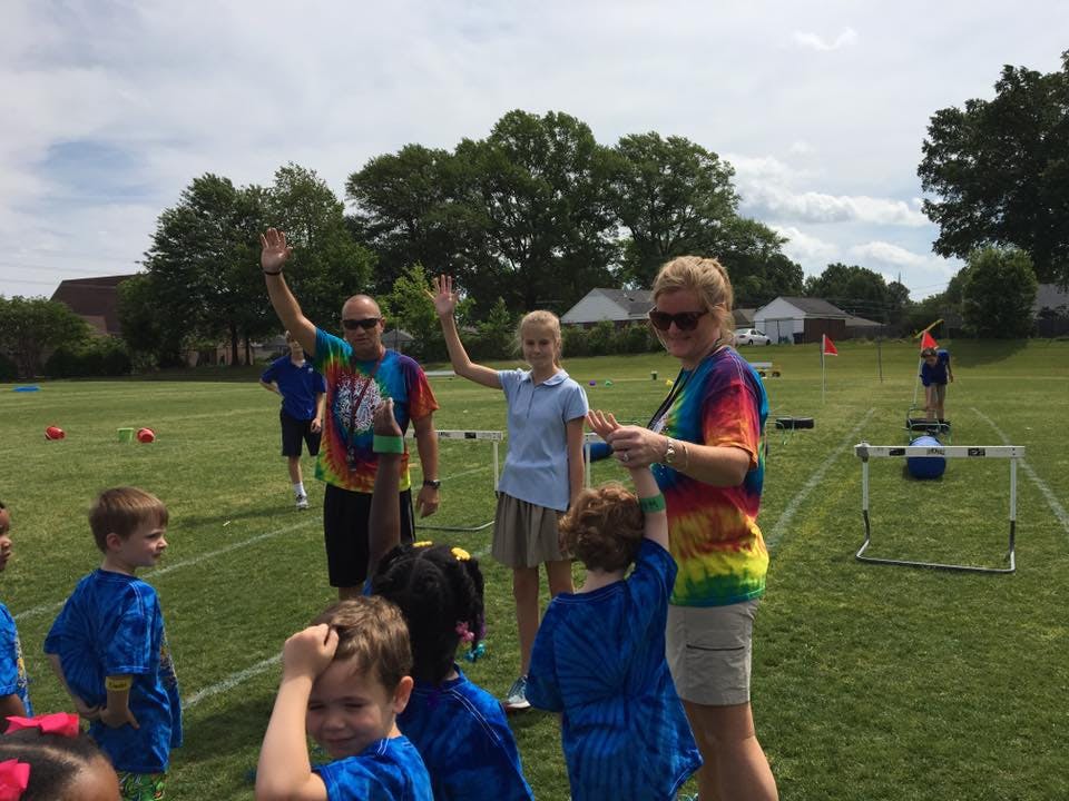 Adults and children on a grassy field, some waving