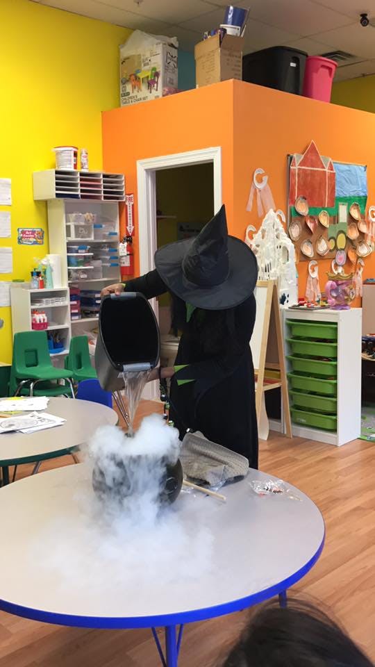 Person in witch costume pouring liquid into a smoking cauldron on a table