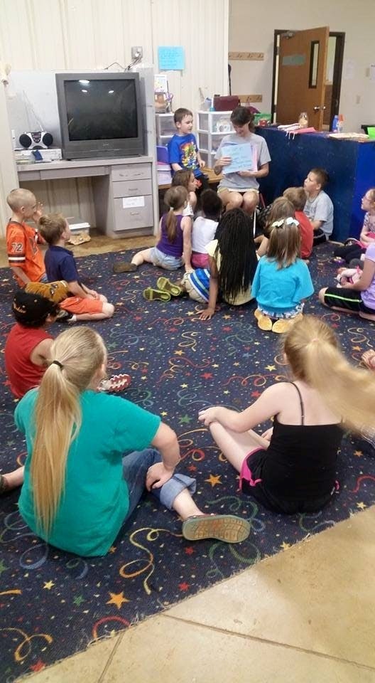 Person reading to a group of children sitting on a patterned carpet