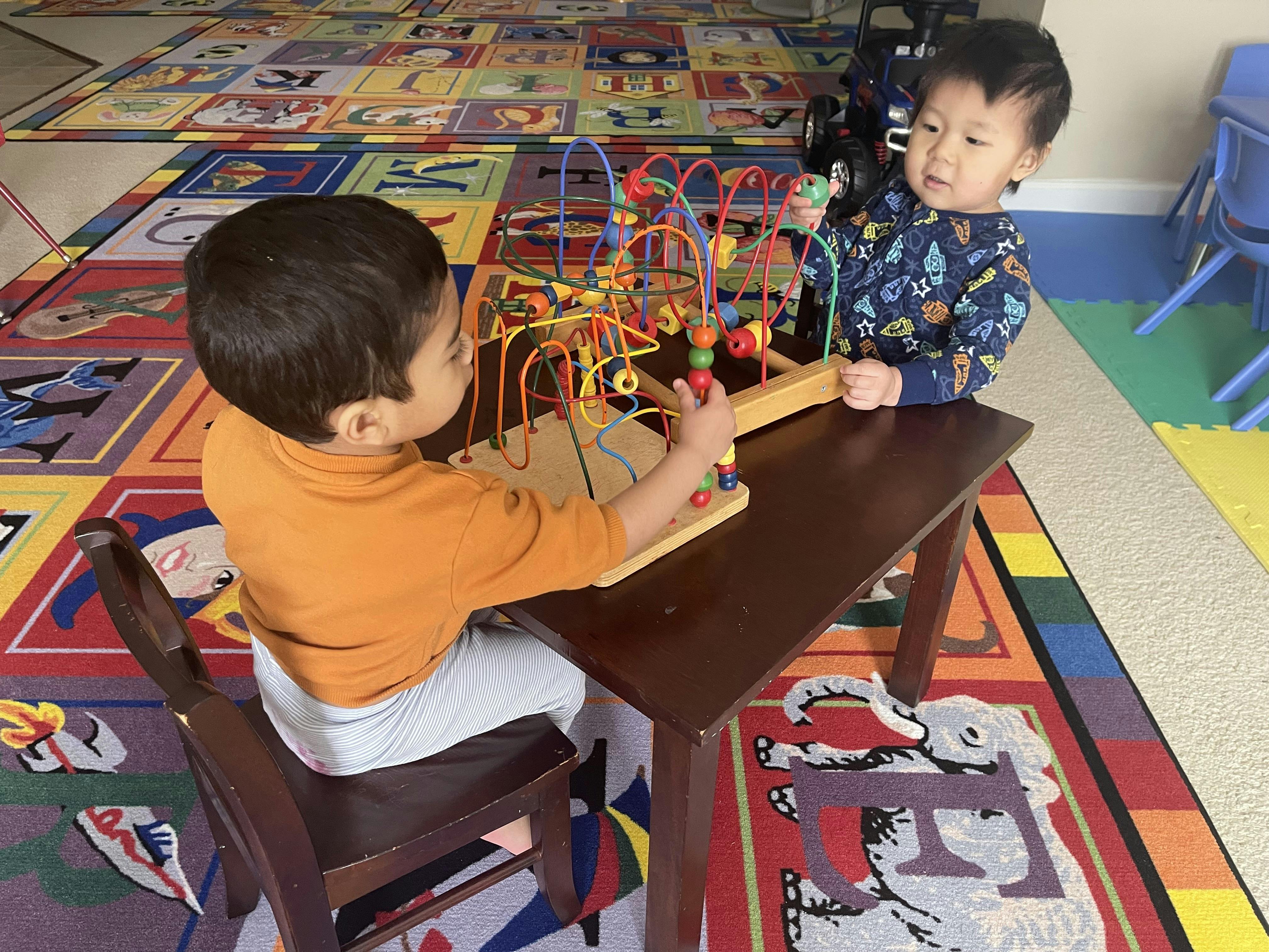 Two children playing with a bead maze toy on a small table