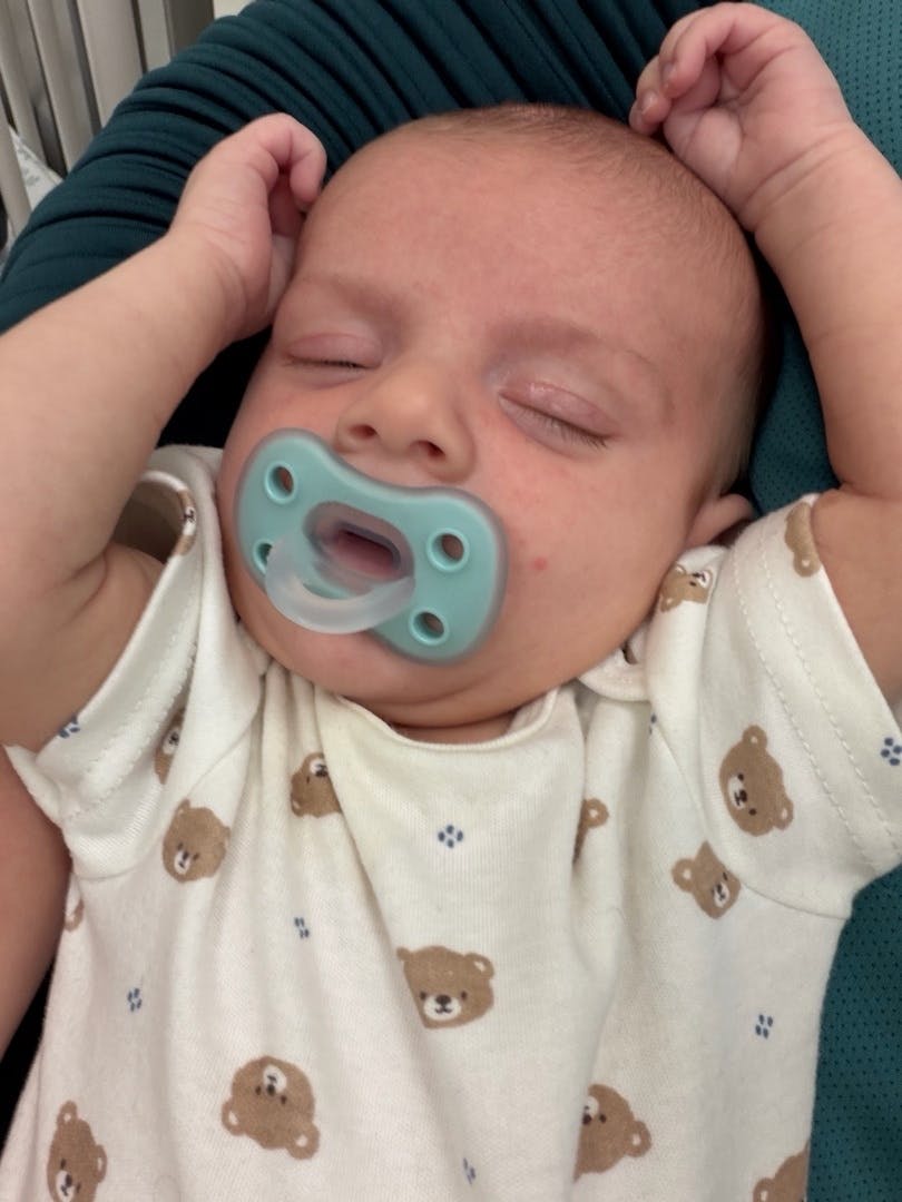 Sleeping baby with a pacifier and hands above head