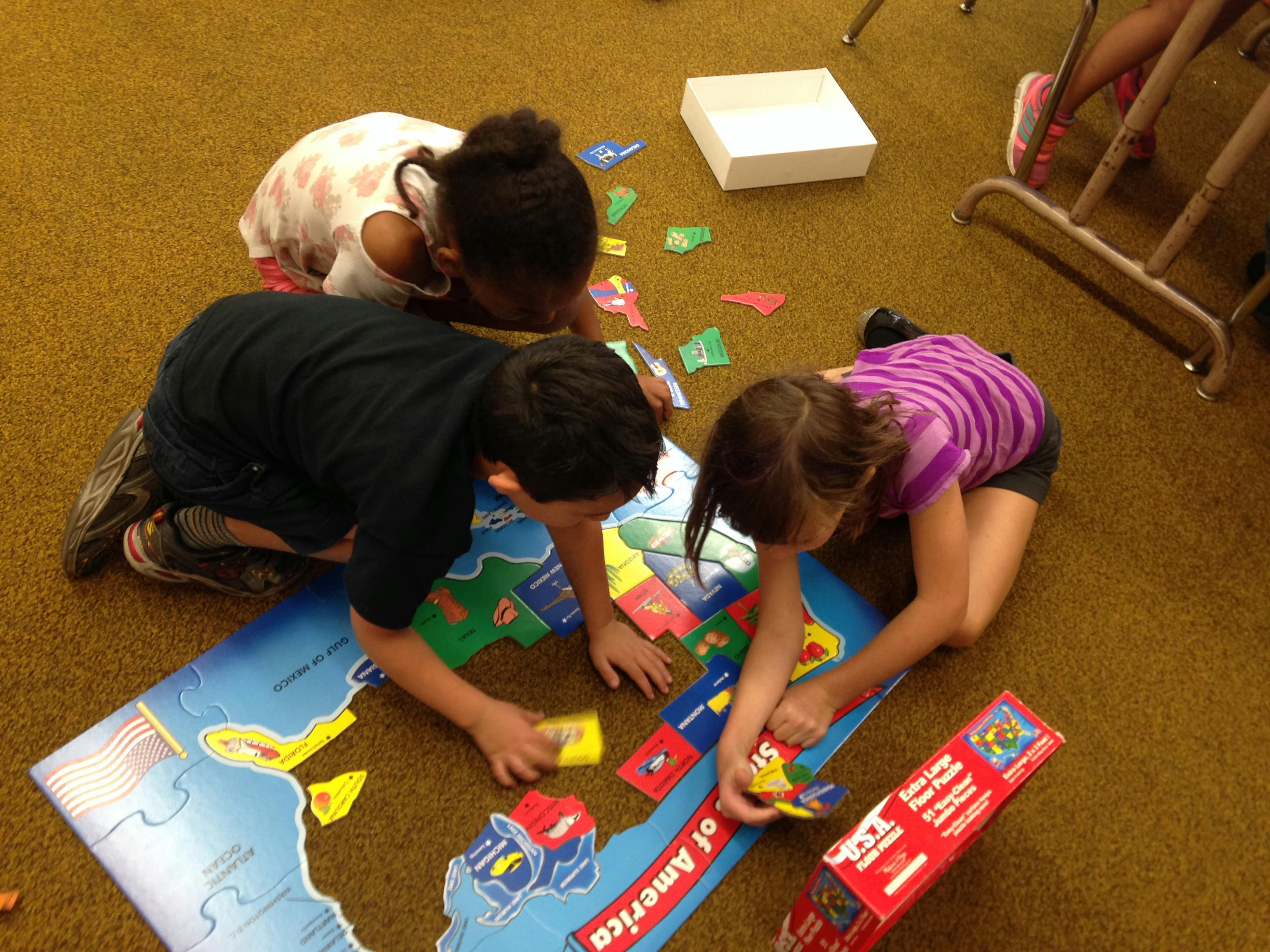 Three children on the floor assembling a large map puzzle