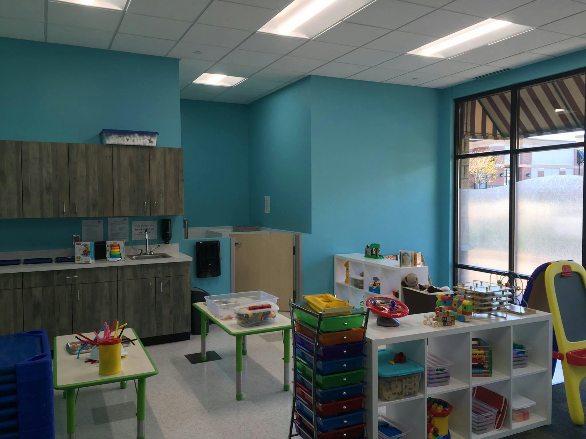 Classroom with blue walls, cabinets, tables, and shelves with supplies