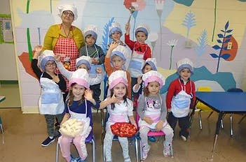 Adult and children in chef hats and aprons posing with food