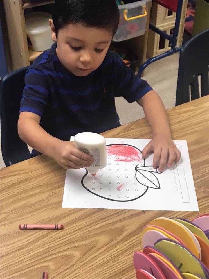 Child coloring an apple outline with a red crayon