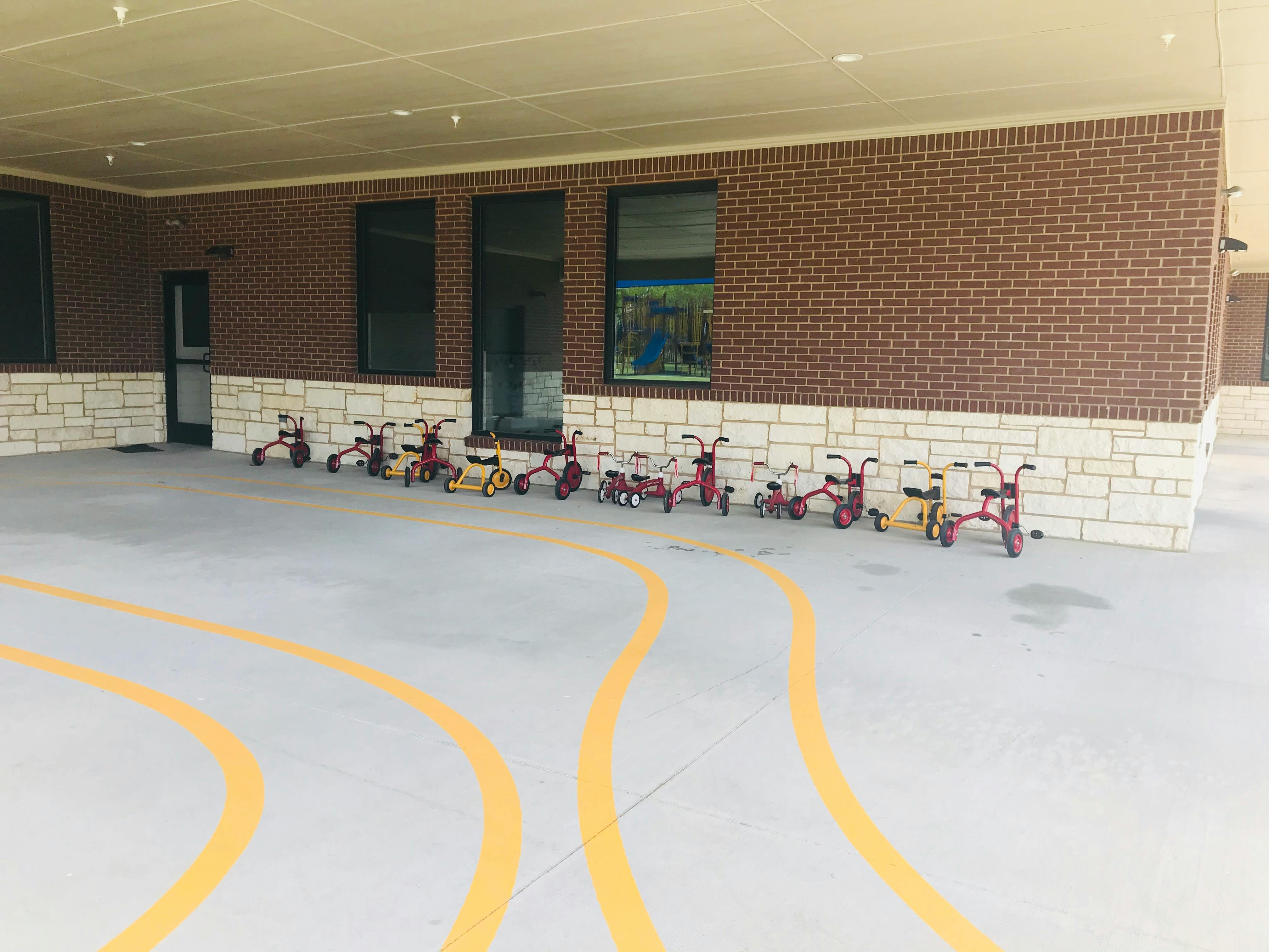 Row of tricycles parked along a brick wall with yellow lines on the ground