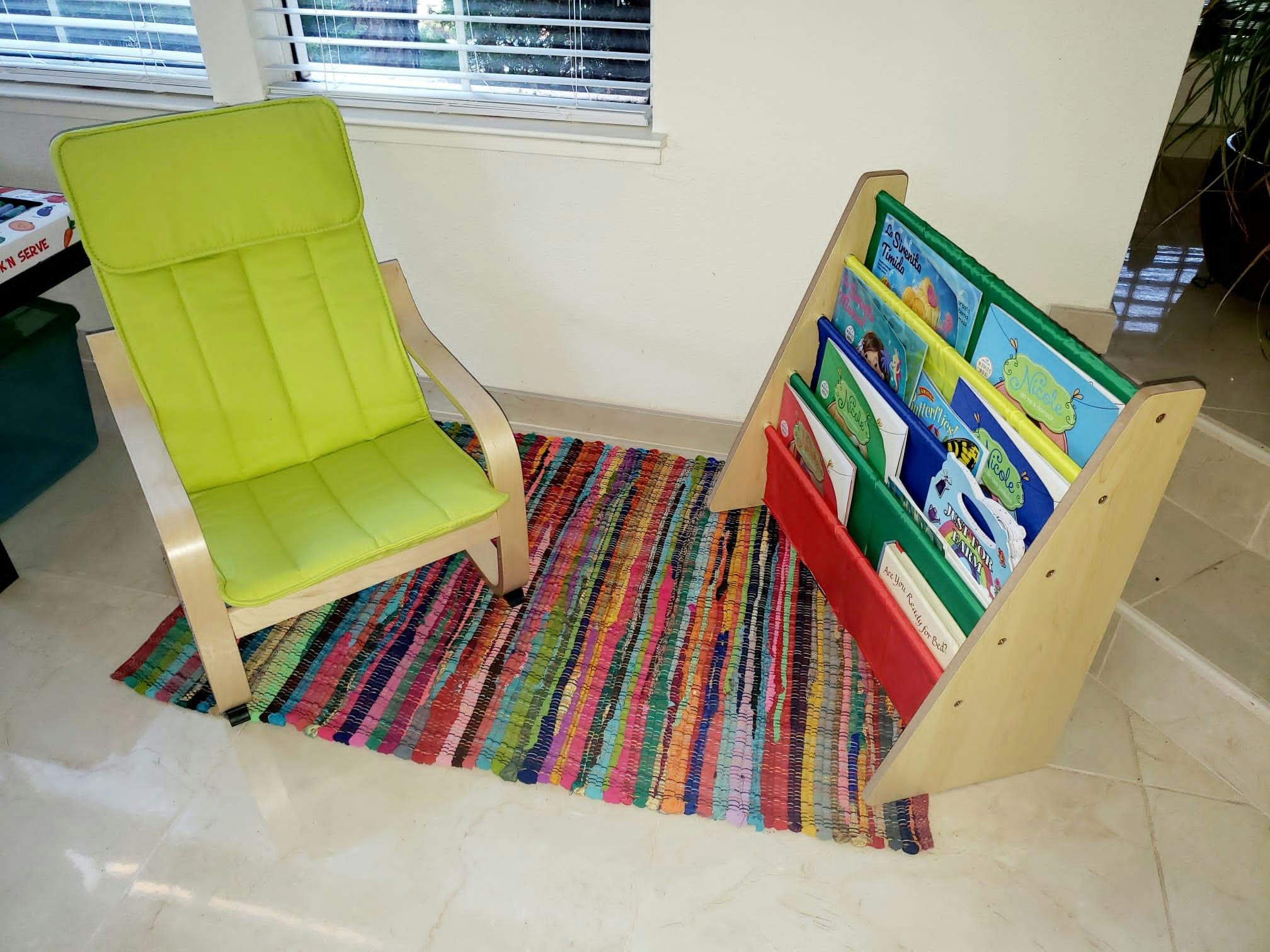 Green chair and a wooden book display with books on a colorful rug