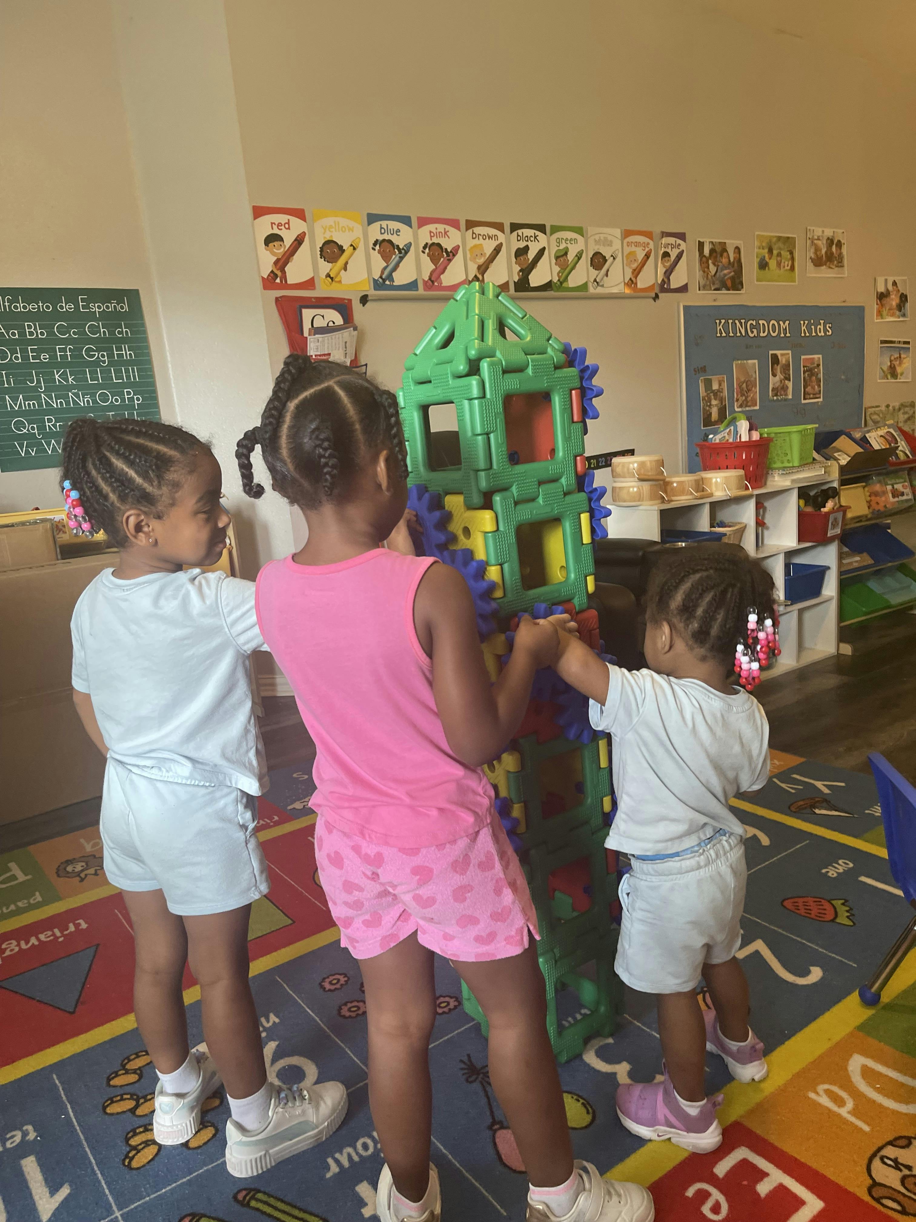 Three children playing with a large plastic building set in a classroom