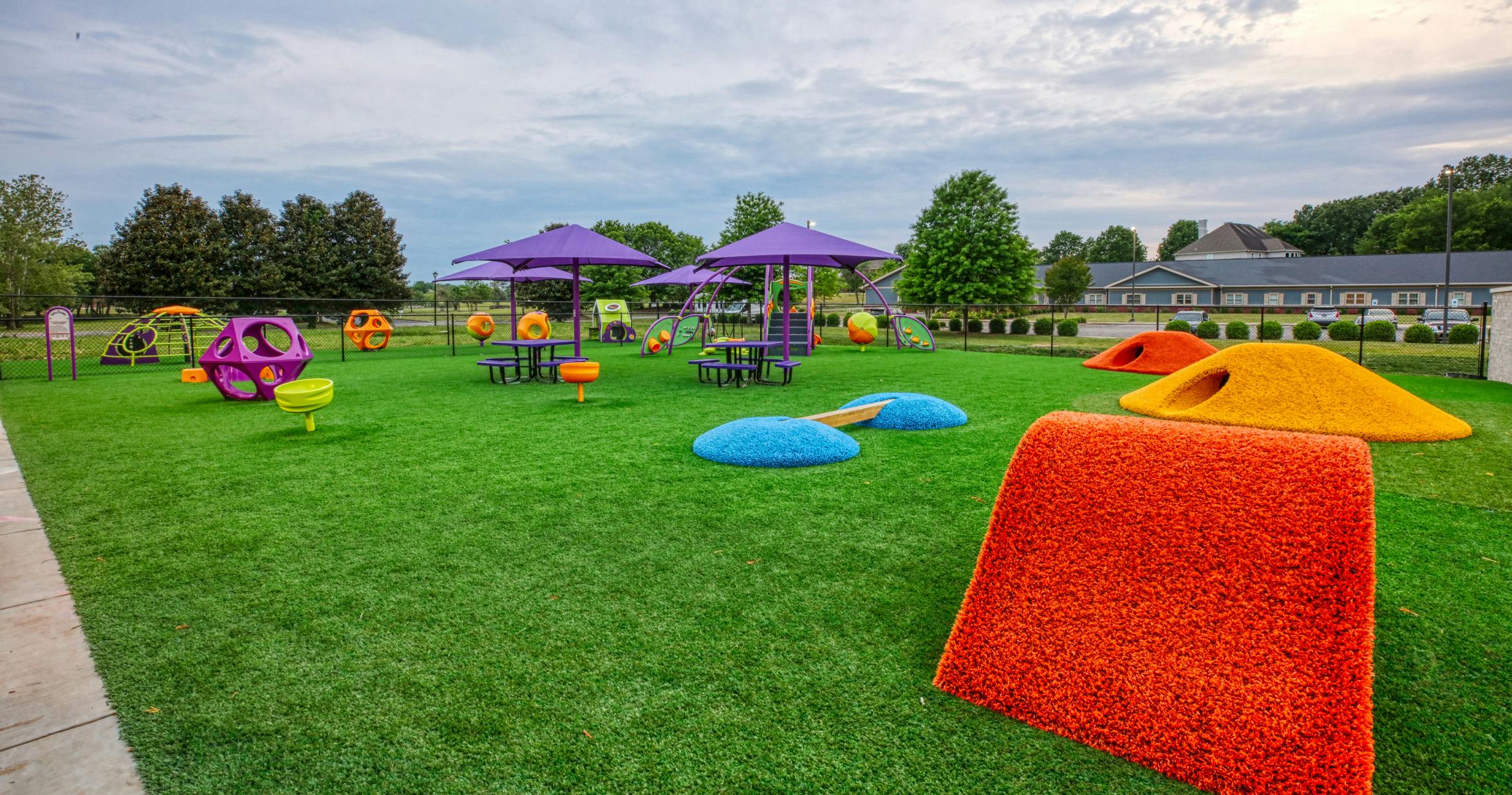 Colorful playground with artificial turf, purple umbrellas, and orange climbing structures