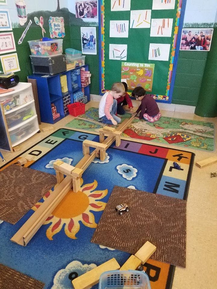 Three children playing with wooden blocks and ramps on a rug