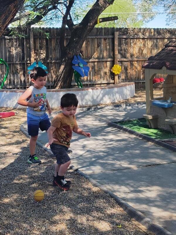 Two children playing outdoors, one kicking a small yellow ball