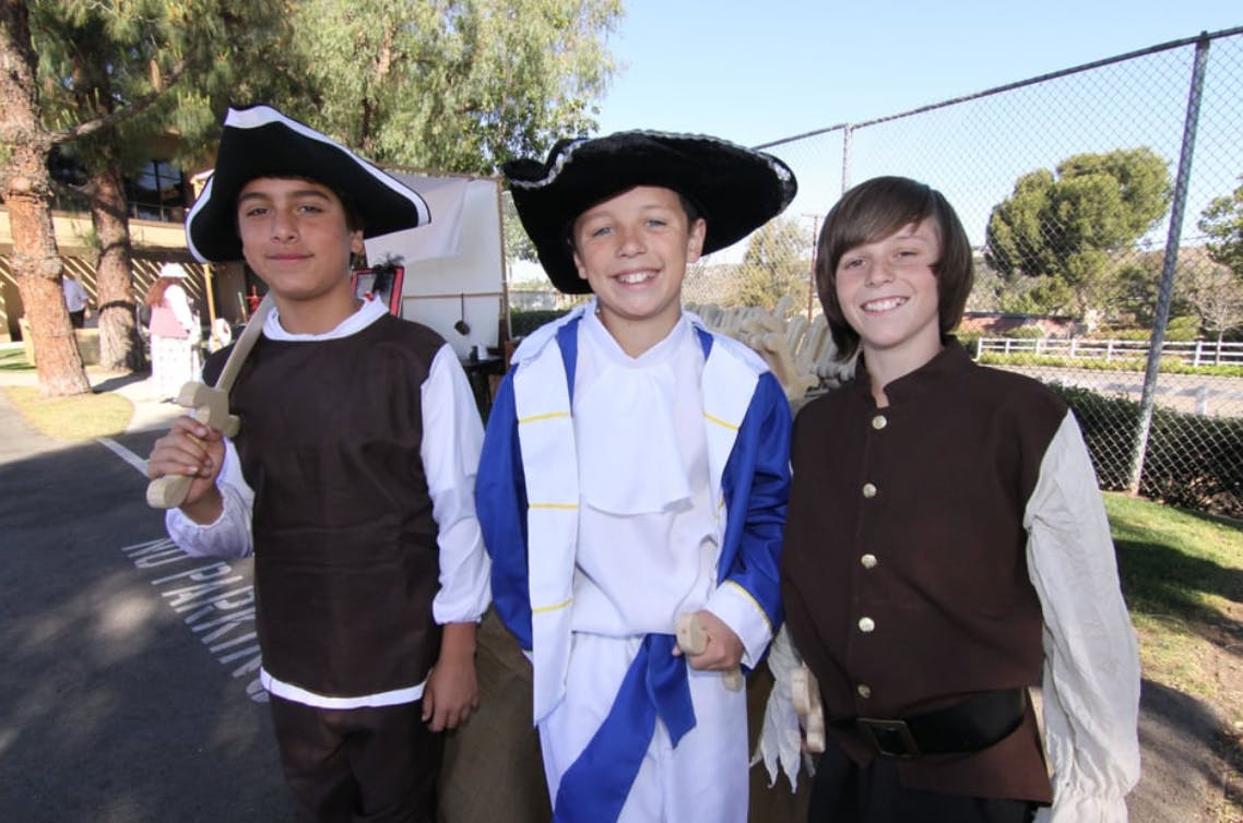 Three children in historical costumes, one holding a toy sword