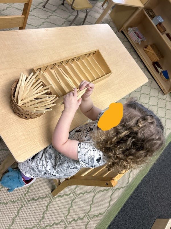 Child playing with wooden counting sticks and a numbered tray
