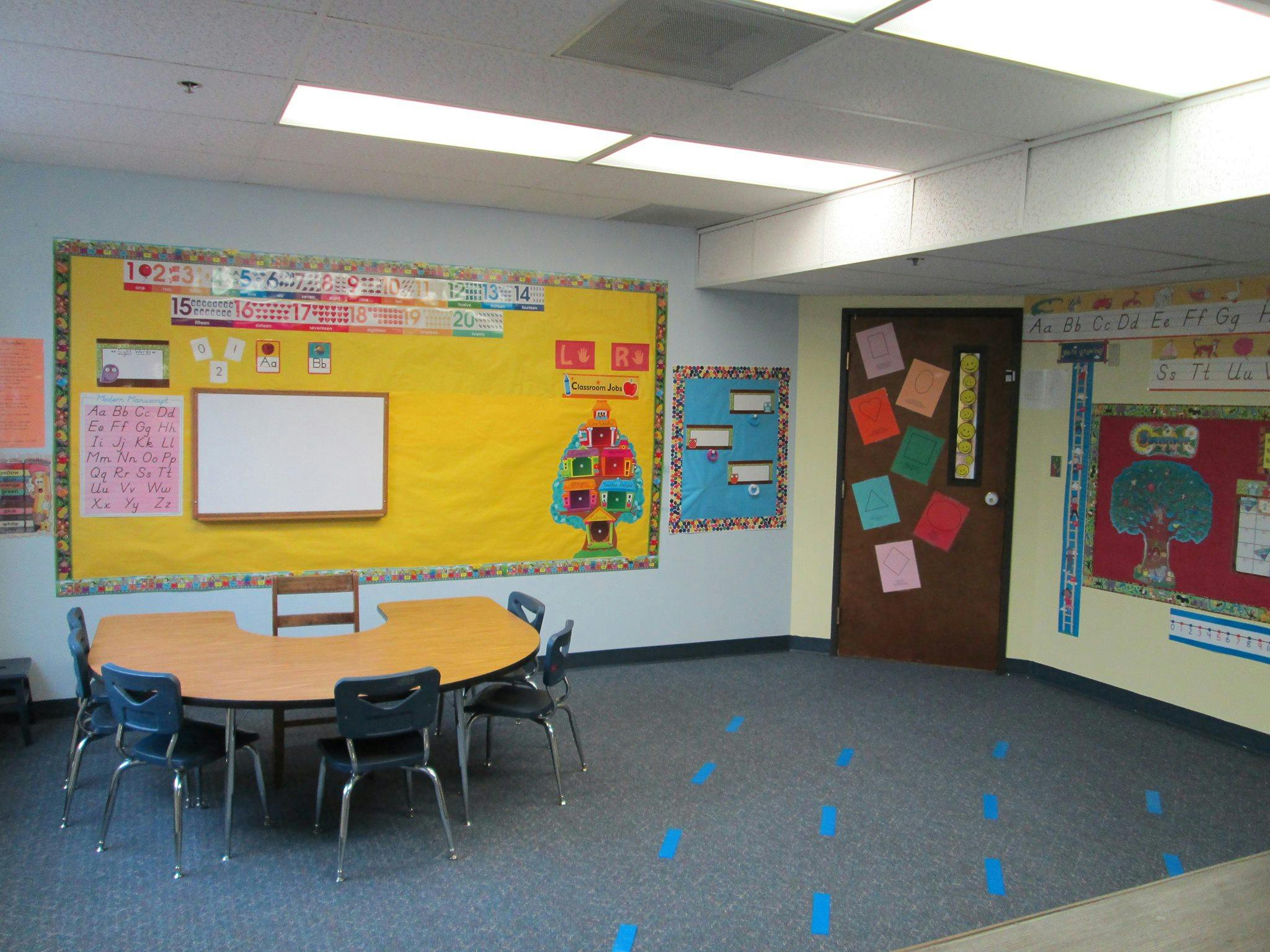 Classroom with a round table and chairs, bulletin boards, and a door